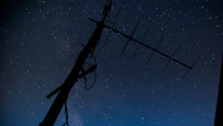 A nighttime shot of a radio antenna tower silhouetted against a starry sky.