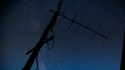 A nighttime shot of a radio antenna tower silhouetted against a starry sky.