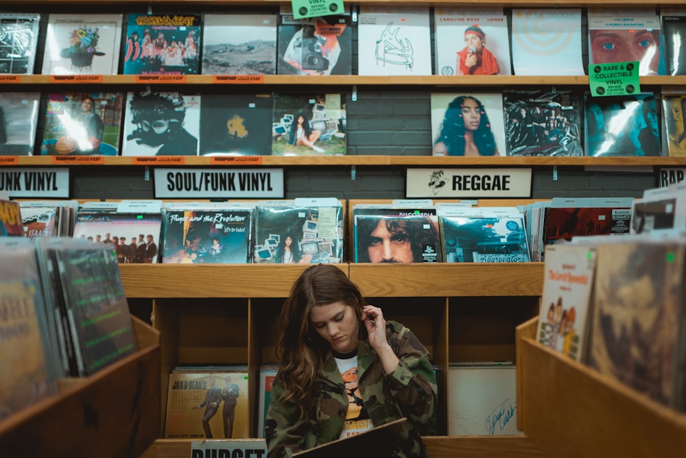 woman in green jacket standing beside books