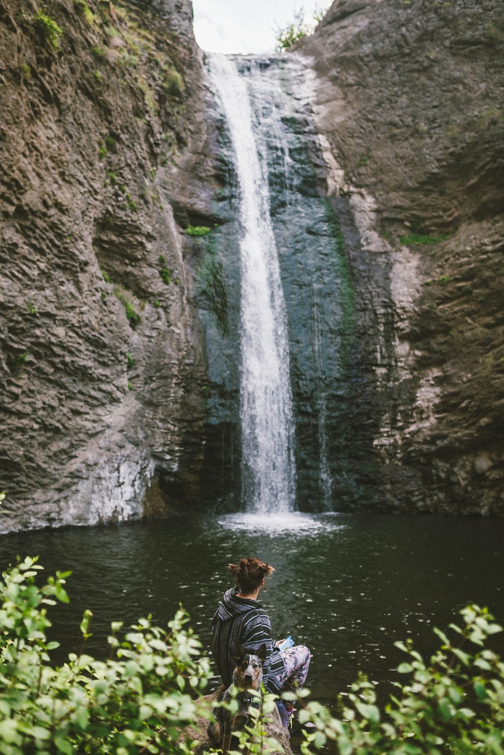 man in black shorts and black shirt standing on rock near waterfalls during daytime