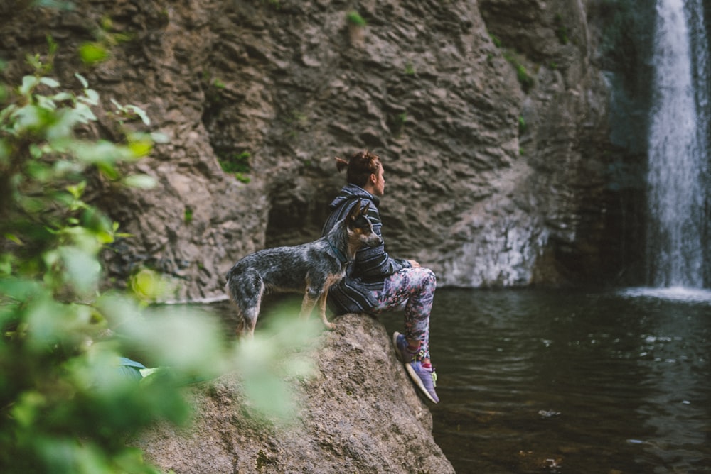 woman in black and white long sleeve shirt and black pants sitting on rock near river