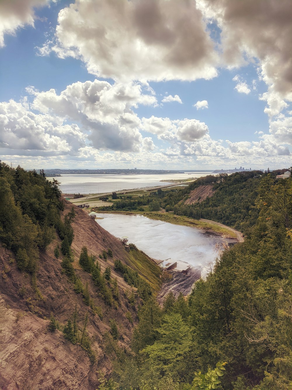 green trees on brown mountain near body of water under white clouds and blue sky during