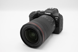 A modern digital camera with a large lens attached, featuring a sleek black design and noticeable branding. The camera is positioned at an angle, showcasing its textured grip and control buttons.