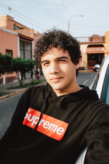 A young person wearing a loose-fitting Booksy hoodie in an urban street setting.