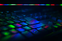 Close-up of hands typing on a keyboard with colorful tech gadgets nearby.