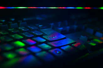 A close-up of hands typing on a keyboard with colorful tech gadgets scattered nearby.