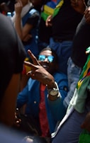 A group of people gathered together with one person in the foreground making a peace sign with their hand. This individual is wearing sunglasses and a blue jacket, creating a focal point with a lively and engaging presence.
