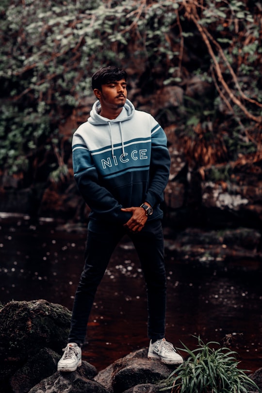 man in blue and white adidas hoodie and black pants standing on rock in water in England United Kingdom