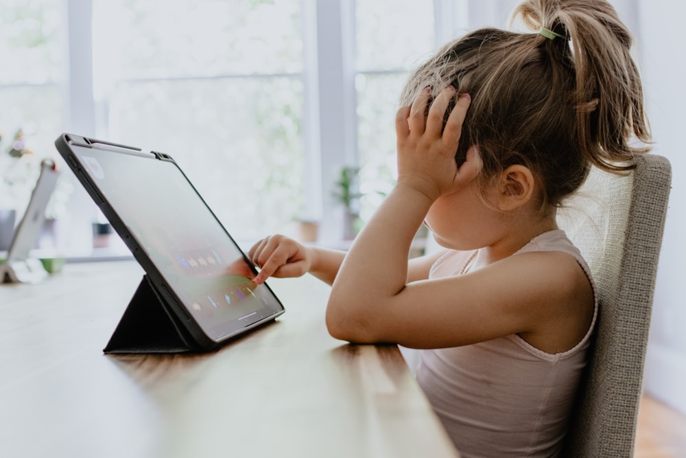 girl in white tank top using black tablet computer