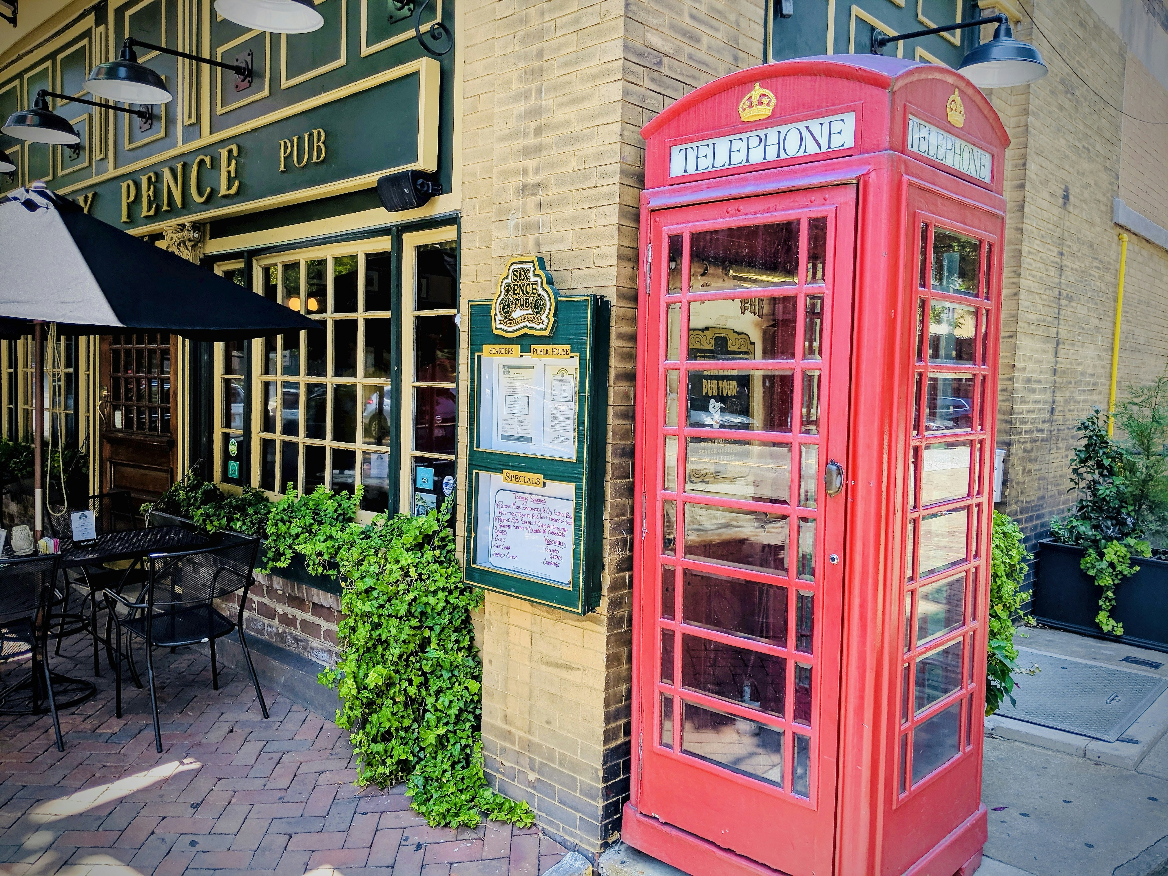 red telephone booth beside brown brick building, Red phone booth found outside the Six Pence Pub in Savannah