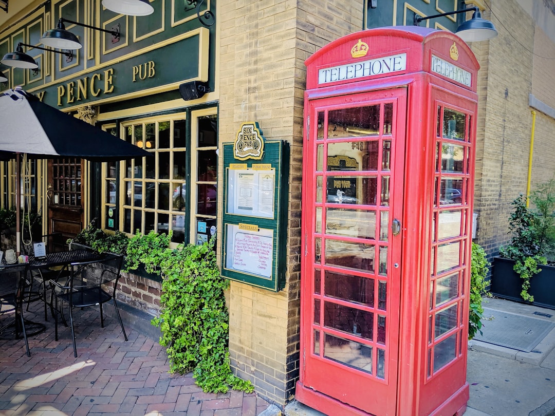 red telephone booth beside brown brick building, Red phone booth found outside the Six Pence Pub in Savannah