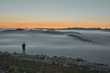 A traveler standing on a cliff overlooking a vast mountain range at sunrise.