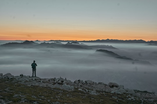 Hiker standing on a rocky cliff overlooking a vast mountain range at sunrise