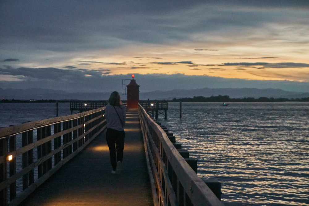 man in black and white long sleeve shirt standing on brown wooden dock during sunset