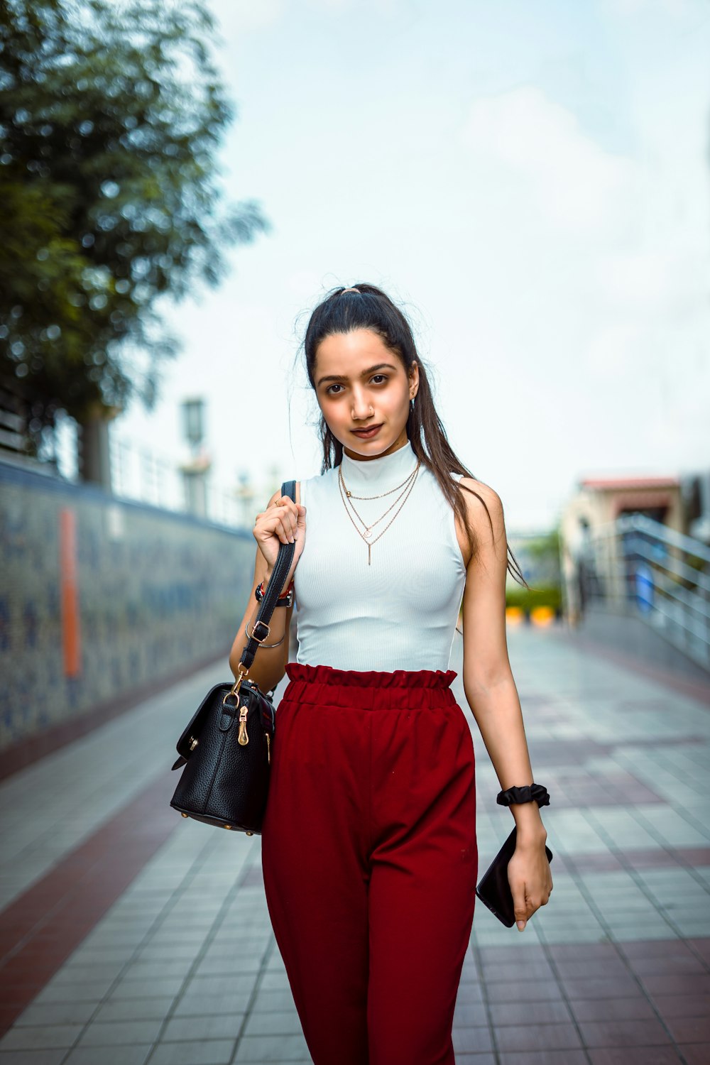 woman in white tank top and red shorts holding black leather handbag