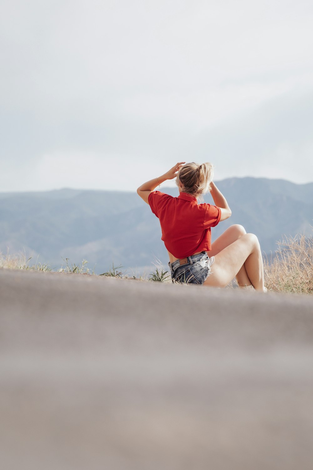 Mujer con camiseta roja y pantalones cortos de mezclilla azules sentada en la roca durante el día