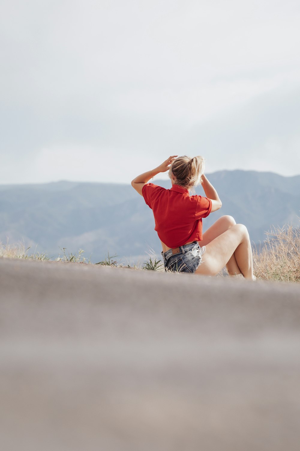 woman in red t-shirt and blue denim shorts sitting on rock during daytime