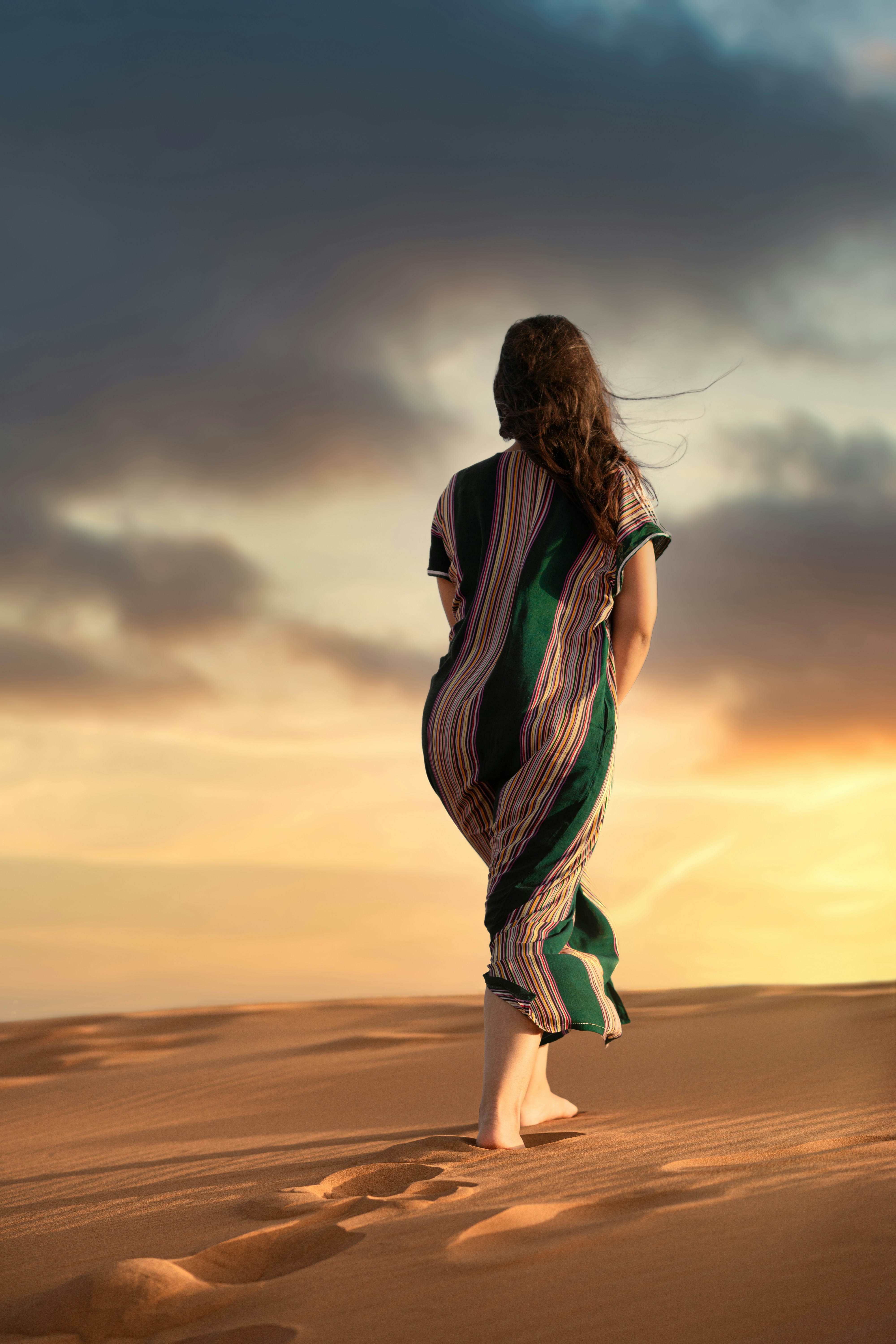 woman in black and green striped dress standing on brown sand during sunset