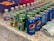 A colorful party setup with a table covered in a confetti-patterned tablecloth. The table is lined with beverages, including cans of Pepsi and Sprite, cartons of apple juice, and small water bottles. A bowl of orange snacks, potentially cheese puffs, is in the background, and a stack of napkins with 'Party Time!' printed on them is in the foreground.