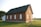 A small, traditional brick church with white-framed arched windows and a steep green roof. It sits on a well-maintained grassy lawn under a clear sky. The building has a quaint, historical charm, with a single red door at the front.