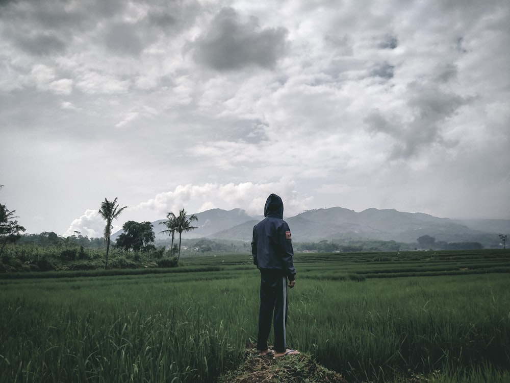 man in black jacket standing on green grass field under gray clouds during daytime