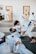 Several individuals are practicing martial arts in a gym setting. They are engaged in a grappling exercise on padded mats, wearing traditional white uniforms with colored belts. The room has doors in the background and appears well-lit.