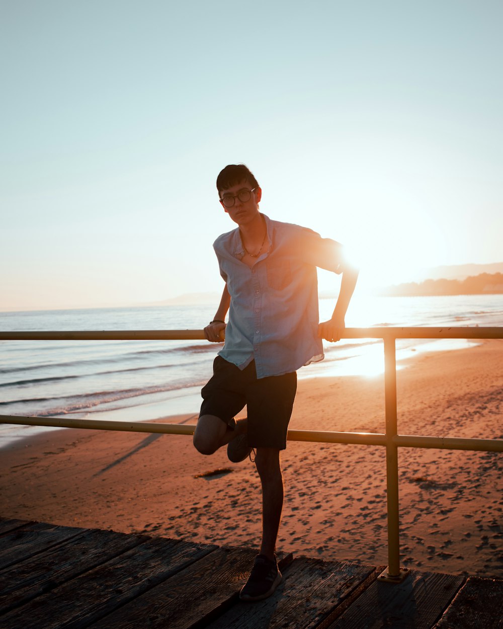 man in white shirt and black shorts standing on beach during sunset