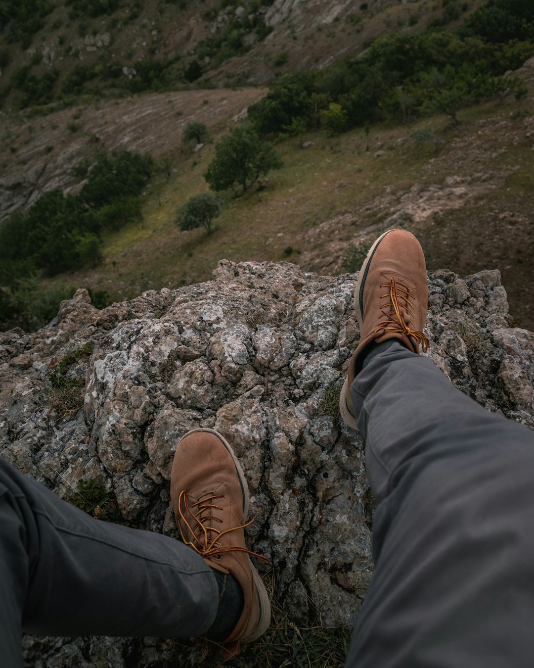person in black pants and brown shoes sitting on rock