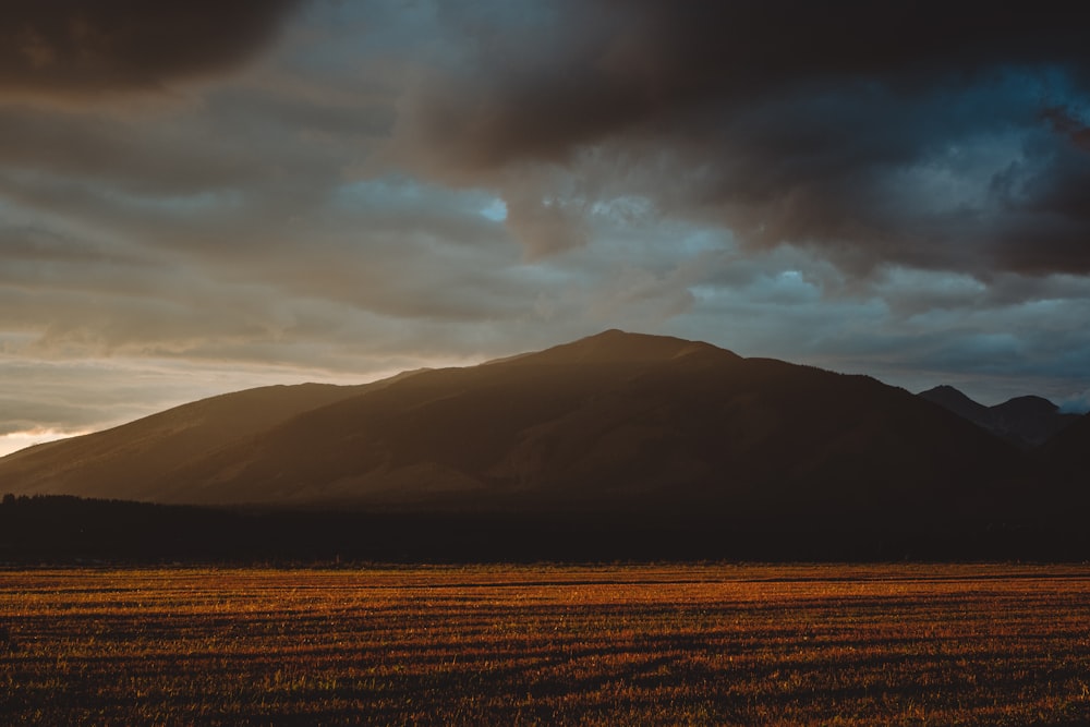 brown field near mountain under cloudy sky during daytime