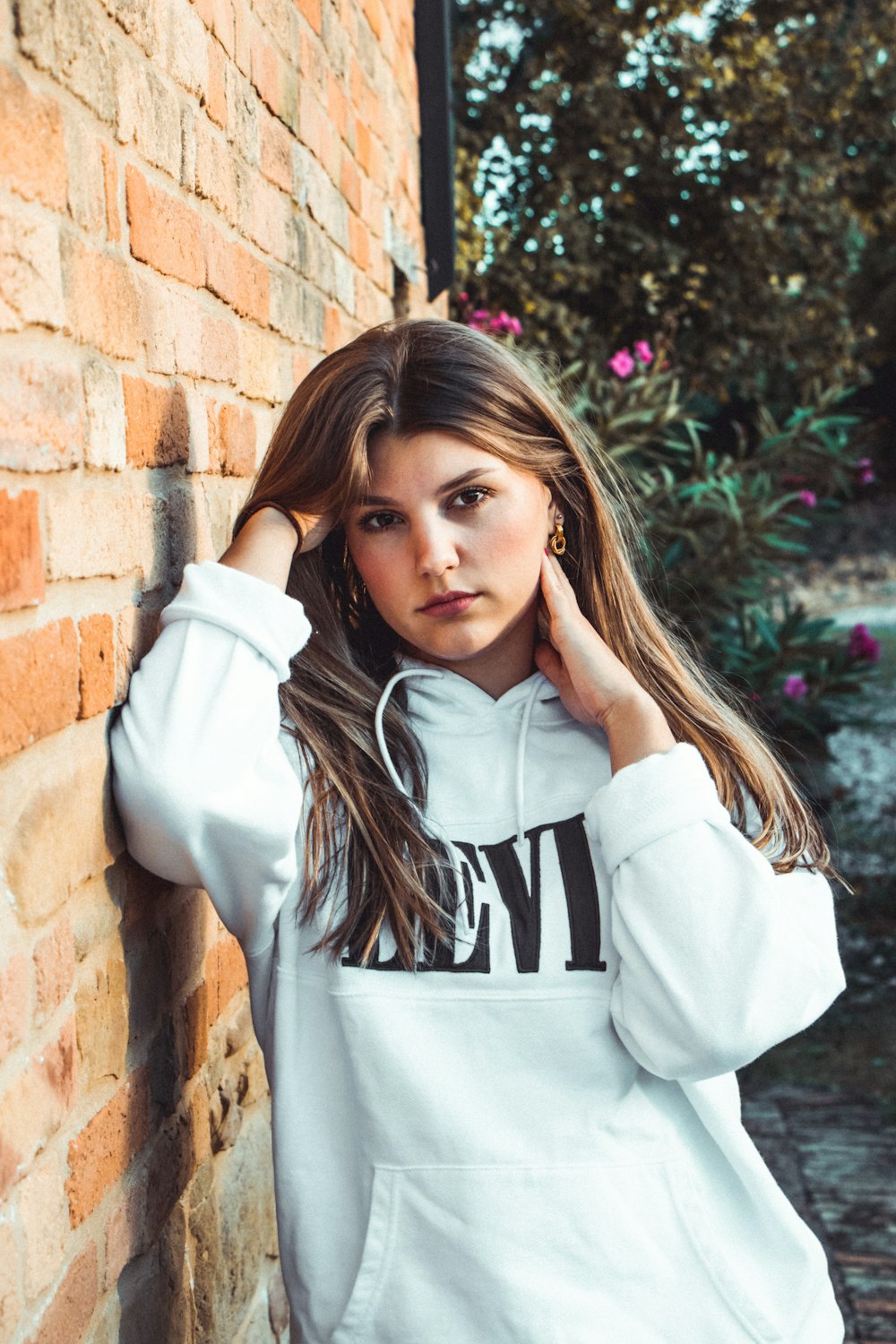 girl in white and black hoodie standing beside brown brick wall