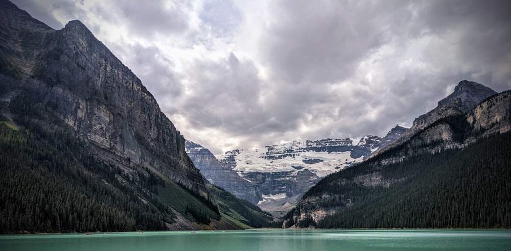 green lake between mountains under cloudy sky during daytime