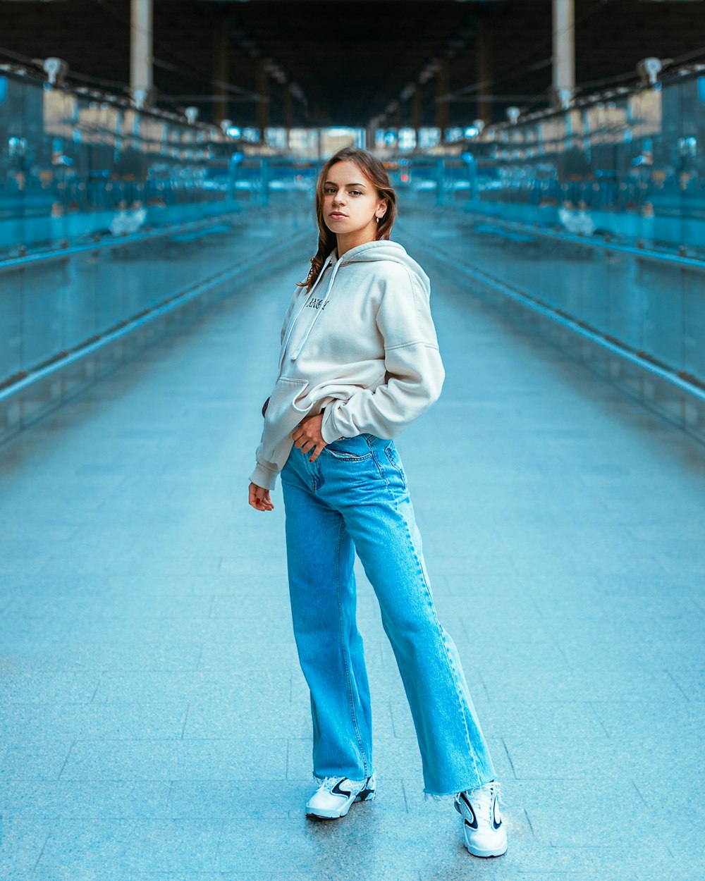 Mujer con sudadera con capucha blanca y jeans de mezclilla azules de pie en el puente
