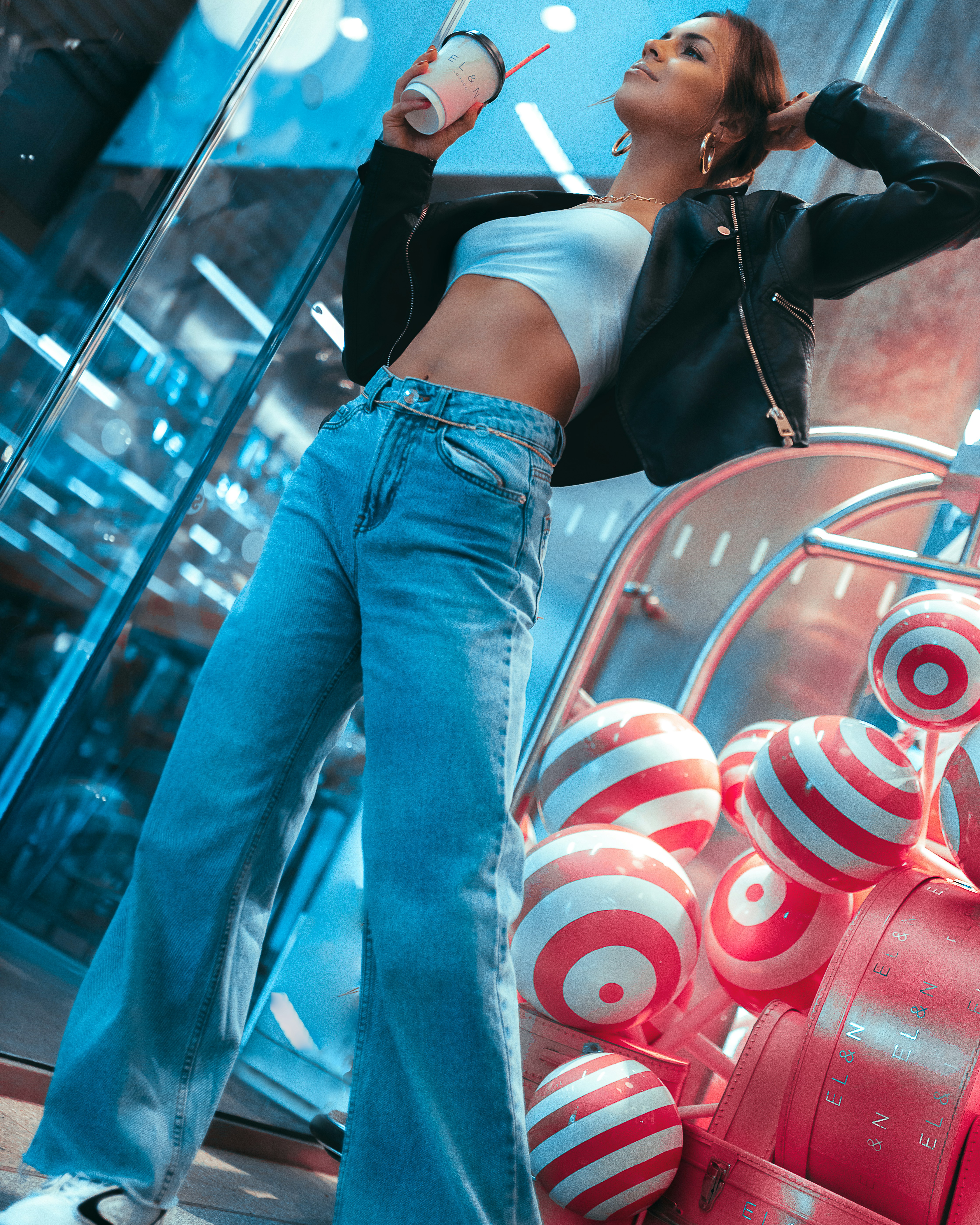 Wanita dengan crop top hitam dan jeans denim biru berdiri di samping kereta merah dan hitam selama