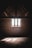 A dimly lit attic with exposed wooden beams and a brick wall. Sunlight filters through a latticed window, casting patterned shadows on the dusty wooden floor.