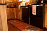 A warm and cozy kitchen with wooden cabinets and a dark countertop. The oven has a towel hanging that says 'Give Thanks'. Various kitchen items are neatly arranged, including a coffee maker and spice rack. The lighting gives a welcoming and rustic atmosphere.