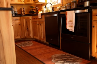 A warm and cozy kitchen with wooden cabinets and a dark countertop. The oven has a towel hanging that says 'Give Thanks'. Various kitchen items are neatly arranged, including a coffee maker and spice rack. The lighting gives a welcoming and rustic atmosphere.
