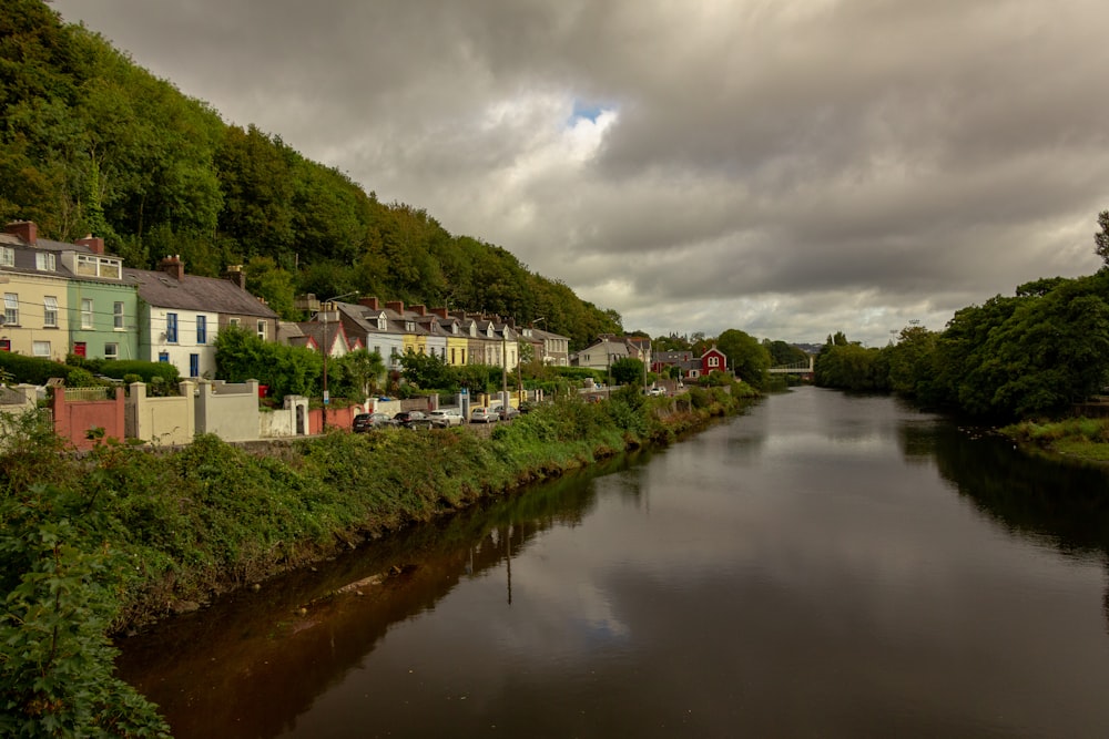 white and gray concrete house near green trees and river under white clouds during daytime