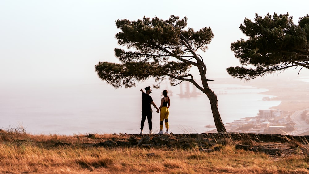 homme et femme debout sur le champ d’herbe brune près de l’arbre vert pendant la journée