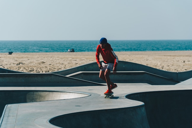 A smiling instructor helping a young student balance on a skateboard near the beach.