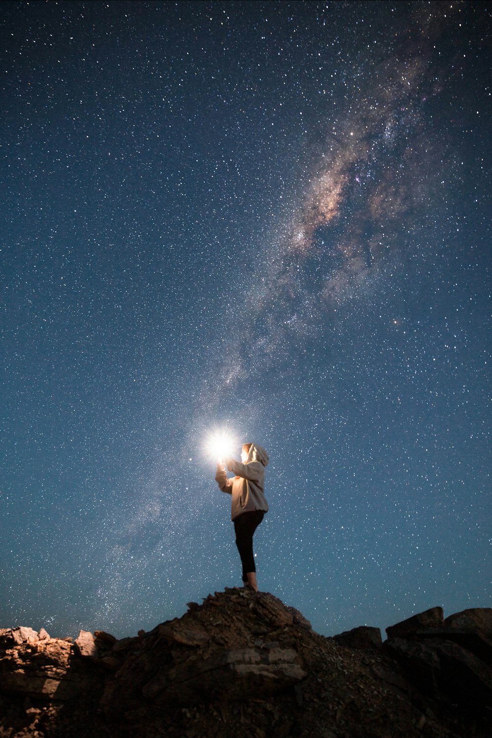 Hombre con camisa blanca y pantalones cortos negros de pie en la roca bajo la noche estrellada