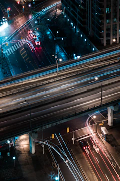 A dynamic aerial view of a bustling urban highway network at dusk, illuminated by streaks of vehicle lights.