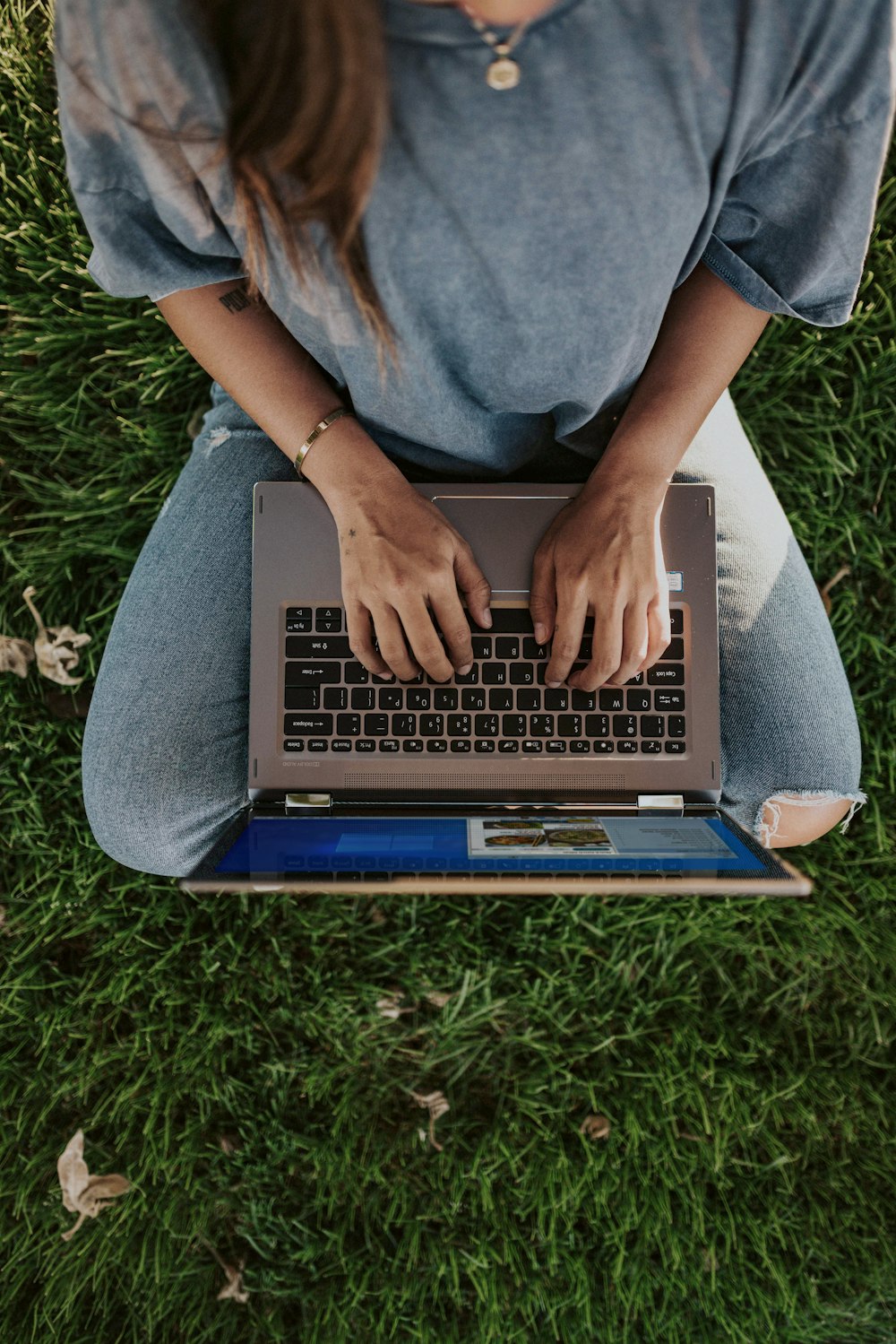 person in blue shirt and blue denim jeans sitting on green grass field using laptop