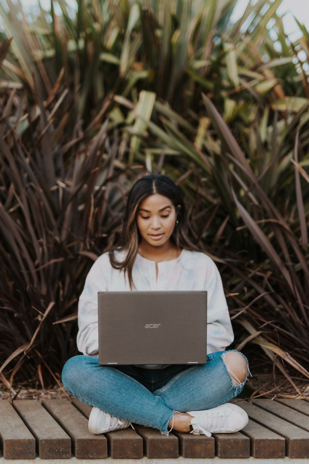 woman in white long sleeve shirt and blue denim jeans sitting on brown dried leaves