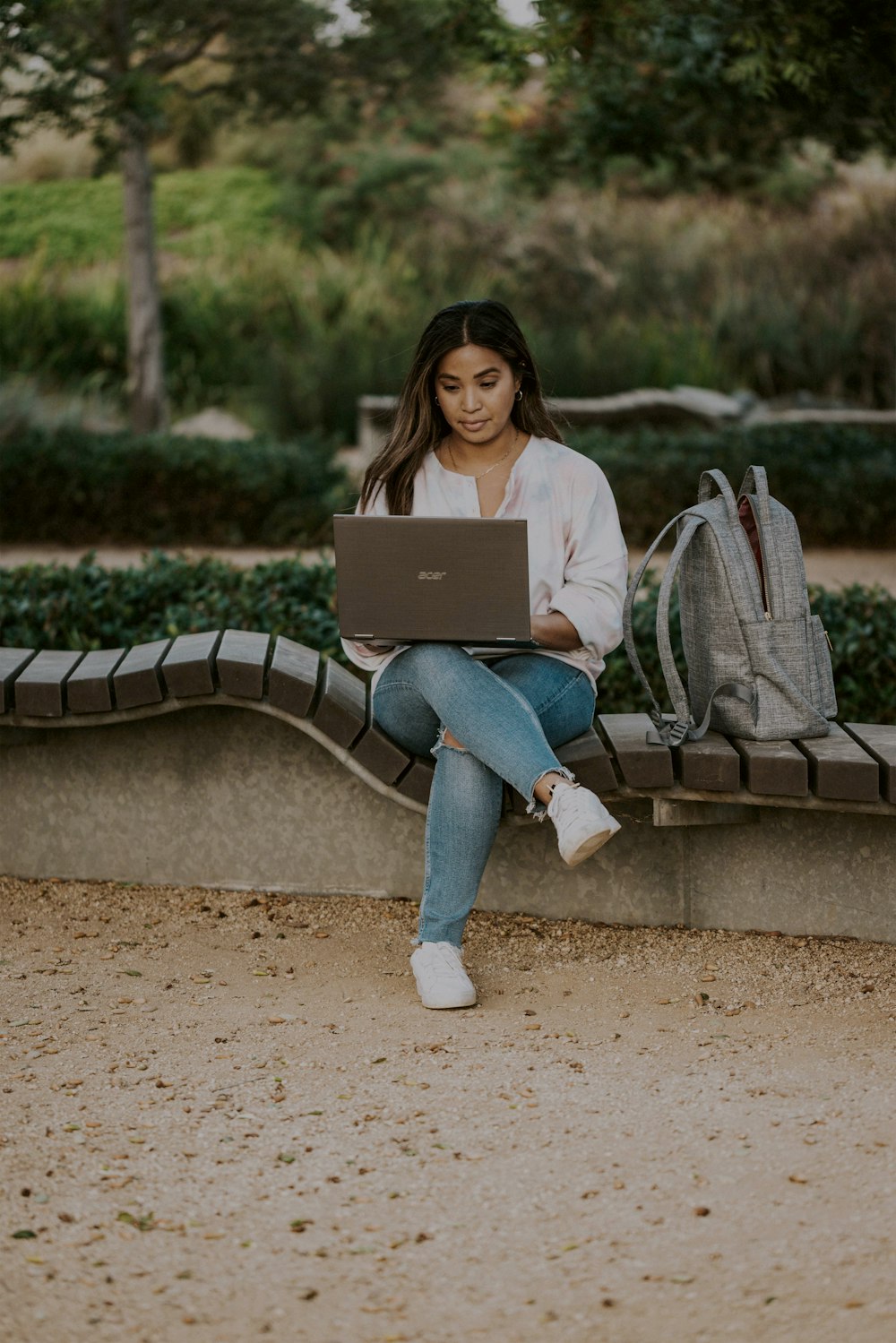 woman in white long sleeve shirt and blue denim jeans sitting on brown wooden bench