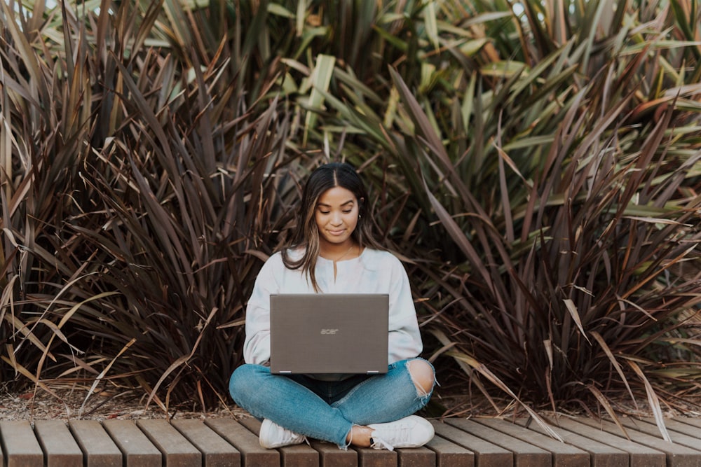 woman in white long sleeve shirt and blue denim jeans sitting on brown wooden pathway