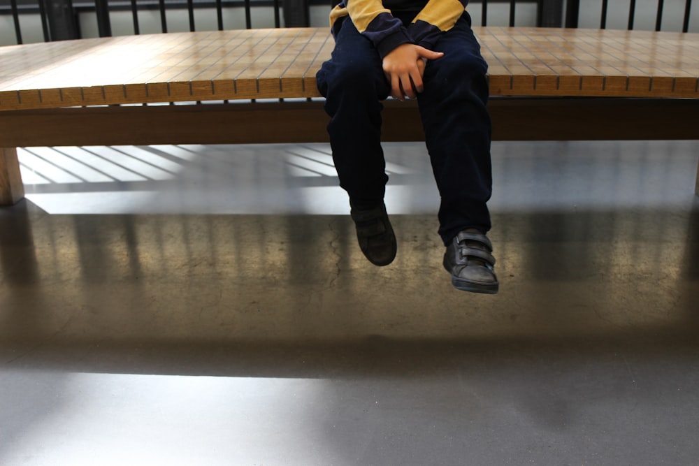 man in black pants and yellow jacket sitting on brown wooden bench