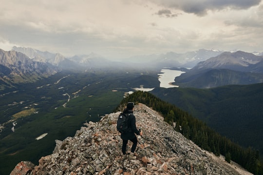 person in black jacket and black pants standing on rocky mountain during daytime in Canadian Rockies Canada