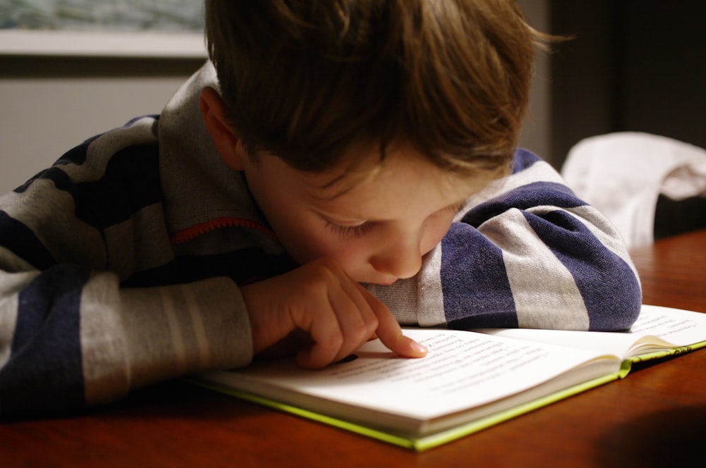 Niño con sudadera con capucha gris y roja leyendo libro