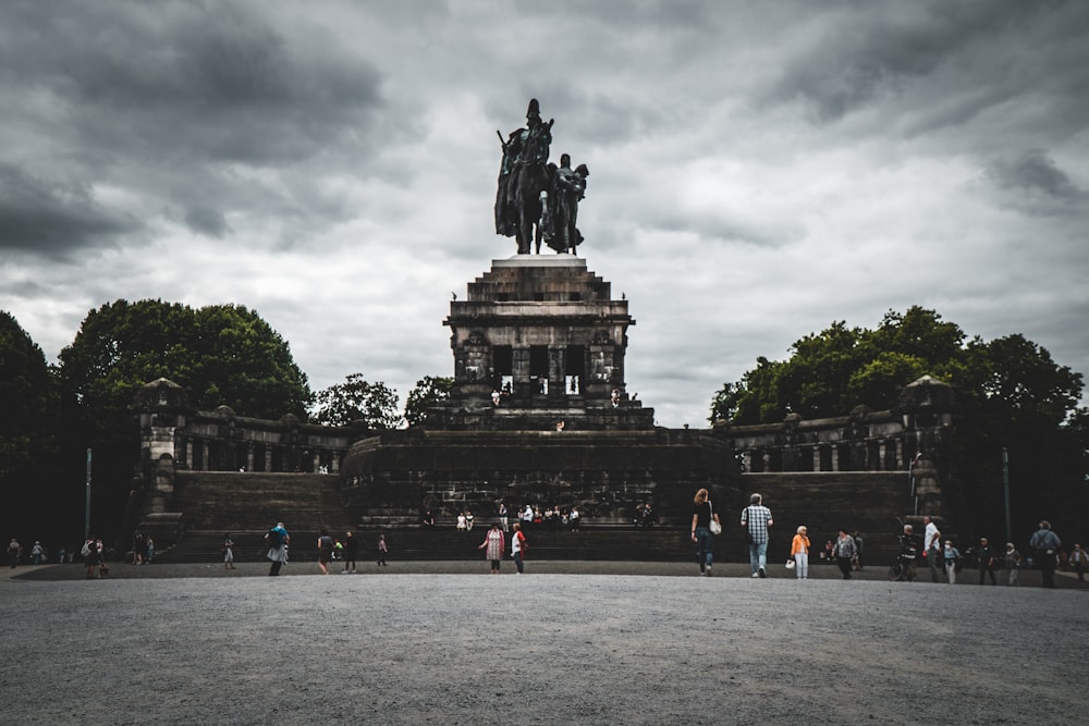 people walking around statue under cloudy sky during daytime