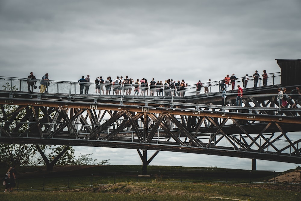 Personnes debout sur un champ d’herbe verte près d’un pont en bois brun sous un ciel nuageux blanc pendant la journée